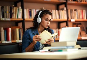 Person with headphones on looking at a computer and holding a book